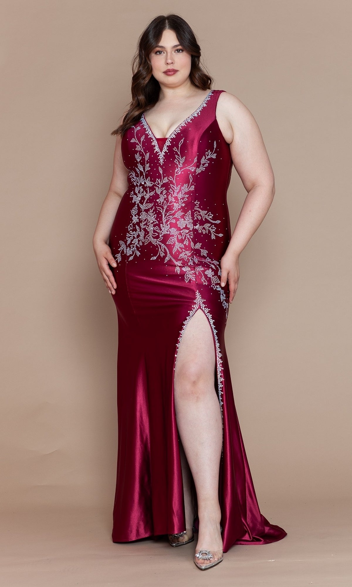 A woman stands against a beige background wearing the Plus-Size Long Spandex Prom Dress with Beads W1132, featuring a deep red hue, silver floral embroidery, a deep V-neckline, and a high side slit for an elegant and sophisticated look.